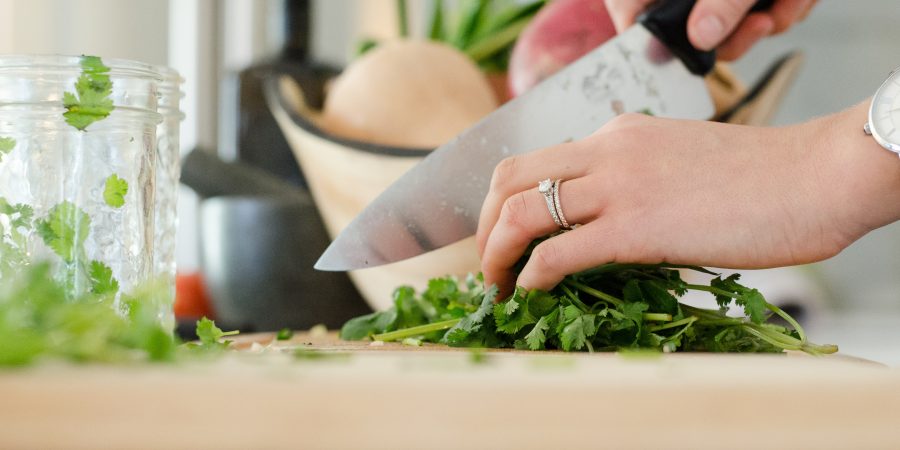 zoom sur les mains d'une personne qui coupe des herbes aromatiques avec couteau de cuisine sur planche à découper